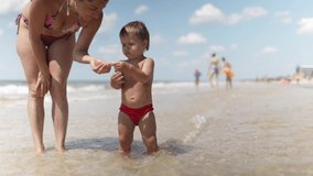 Little funny funny kid, collects shells and pebbles in the calm blue sea on a sandy bottom together with caring kind beautiful mother under the hot summer sun on bright vacation. 4K UHD slow-mo video - Powered by Shutterstock - Get 15% off with code: PIKWIZARD15
