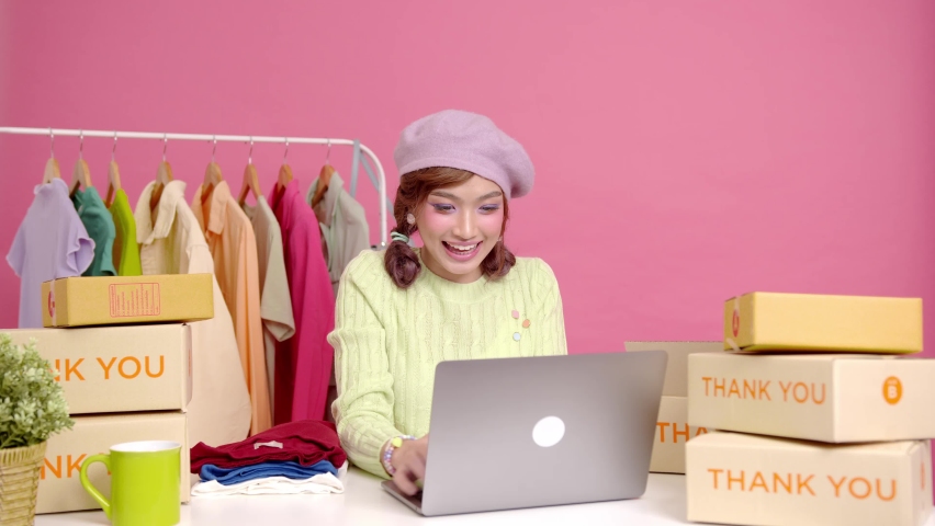 Young asian woman startup small business freelance sale fashion clothing with parcel box and computer laptop on table and sitting isolated on pink background. Online marketing and delivery concept. Royalty-Free Stock Footage #1096101819