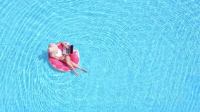 Beautiful young woman with pink inflatable ring relaxing in swimming pool. top view. Girl in the pool swims on an inflatable donut of pink color using app on mobile tablet device
 - Powered by Shutterstock - Get 15% off with code: PIKWIZARD15