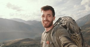 SLOW MOTION, CLOSE UP: A happily smiling Attractive man records a video on the camera. he talks about his magnificent and interesting journey and points to the mountain with his hand