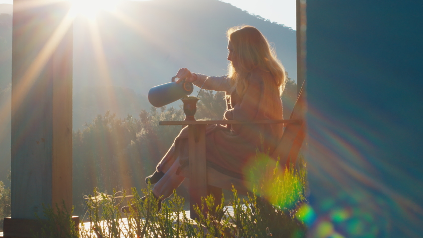 Woman drinks mate tea and enjoys sunrise in Brazilian mountains from the wooden terrace