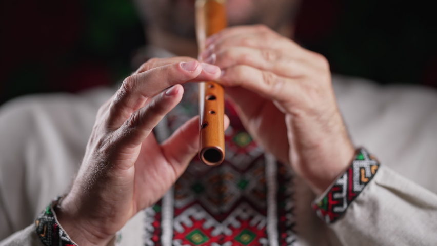 Hands of man playing on woodwind wooden flute - ukrainian sopilka on dark background. Folk music concept. Musical instrument. Musician in traditional embroidered shirt - Vyshyvanka. | Shutterstock HD Video #1096119537