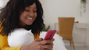 Cheerful brazilian hispanic latin young woman relaxing on bed using mobile phone. High quality 4k footage