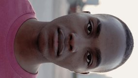 Close up vertical portrait of black african american young man standing outdoors - Portrait of cheerful colombian teenager boy in city street. Slow motion high quality HD footage