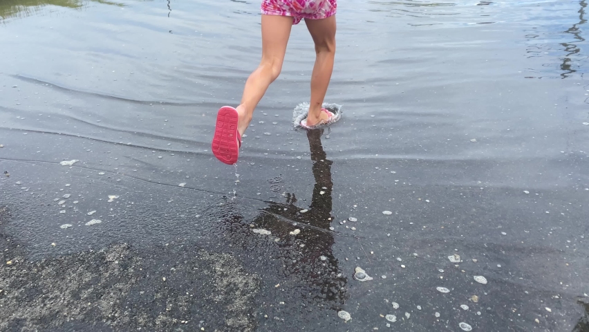 young girl splashing with a dress and flip-flops on a flooded suburban seaside community
