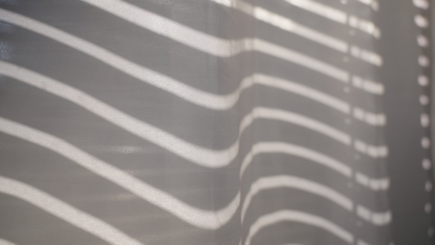 Window shutters or blinds open up creating shadow lines on white curtain. Dark to light sun enters the room as blinds swing open drawing shadow on closed curtain indoor | Shutterstock HD Video #1096132463