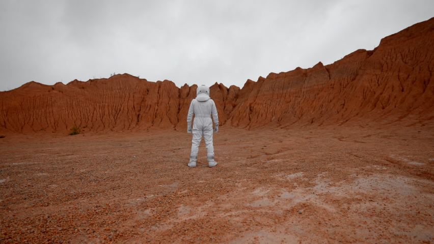 A cosmonaut in a white suit stands inside the crater and looks ahead. Rear view of an astronaut inspired by a landscape from a distant planet.