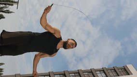 Vertical video. A young man jumps on a skipping rope outdoors in front