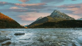 Cinemagraph seamless video loop of a mountain river in the Austrian alps with a vibrant evening sky, close to the German border in autumn. The water is rushing along colorful fall trees. 4K UHD.