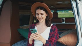 Portrait of attractive cheerful young Caucasian woman holding smartphone and texting. Portrait of happy girl in red plaid shirt near camping car and using mobile phone. Outdoors. Tourism concept - Powered by Shutterstock - Get 15% off with code: PIKWIZARD15