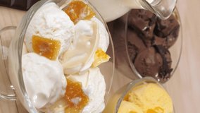 Vertical video. Three glass jars filled with ice cream balls with vanilla, chocolate, mango and banana flavors. A woman's right hand is lowered with a teaspoon to take vanilla ice cream.