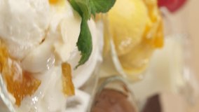 Vertical video. Three glass bowls filled with ice cream balls with flavors of ice cream, chocolate, mango and banana are spinning in front of the camera. Stops at yellow ice cream.