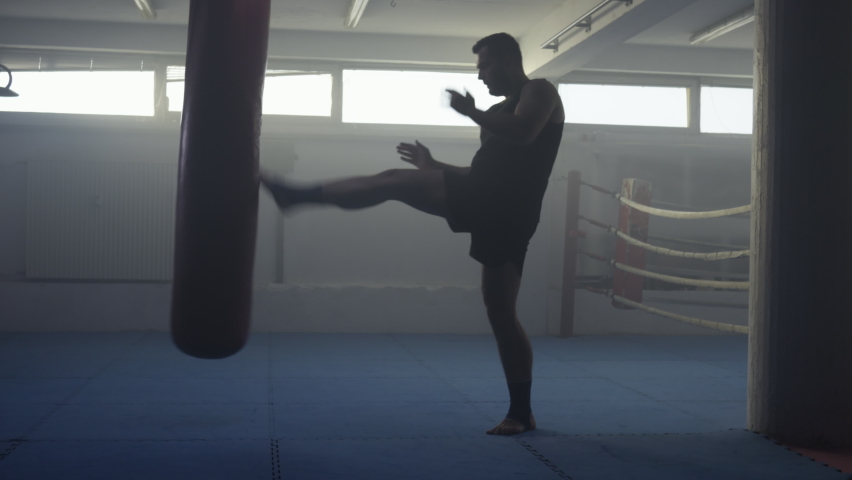 Kickboxer exercising with boxing pear, training punches in fighting club, wide shot. Fighter gym workout, mid adult sportsman practicing hand and leg kicks, wide shot