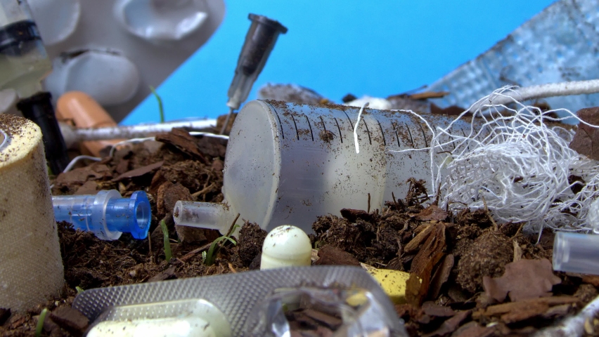 Medical waste pile lying on the ground in forest where fresh green grass is growing in timelapse. Macro landscape of polluted lawn by used syringes and bandages. Problems of planet conservation