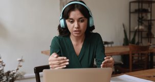 Female counsellor wear headphones talks to client, provide support, take part in video call, remote talk use application working in office sit at desk look at laptop screen. On-line consultation event