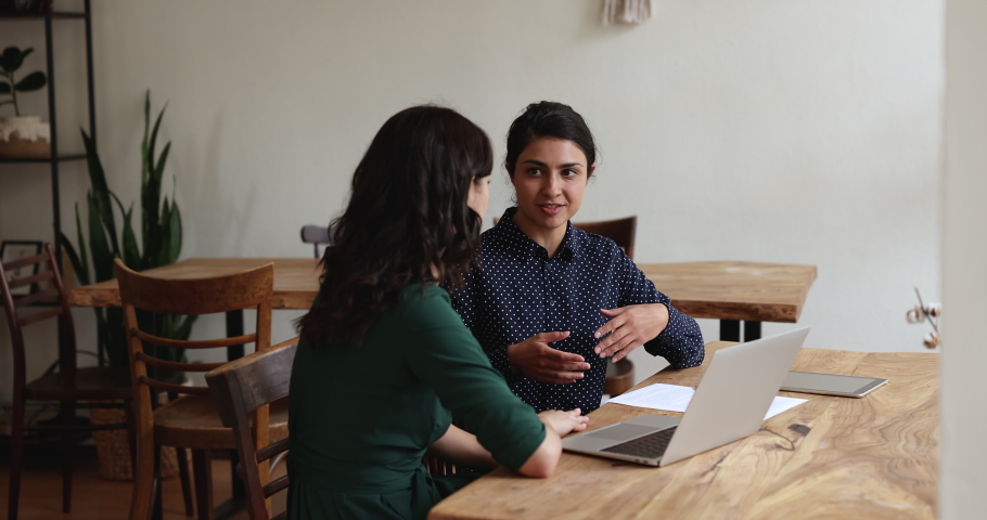 Indian woman explains to colleague vision of collaborative project sit together at desk share ideas talking solve common task. Sales manager meet with client, offering services of company in office | Shutterstock HD Video #1096165033