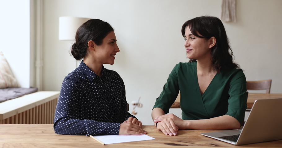 Two multi ethnic businesswomen shake hands after making profitable deal feel satisfied sit at desk with signed documents and laptop in modern office. Sales manager and client accomplish formal meeting Royalty-Free Stock Footage #1096165133