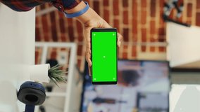 Vertical video: Female freelancer looking at smartphone with greenscreen, analyzing horizontal chroma key display with isolated copyspace. Using blank mockup template on mobile phone. Tripod shot.