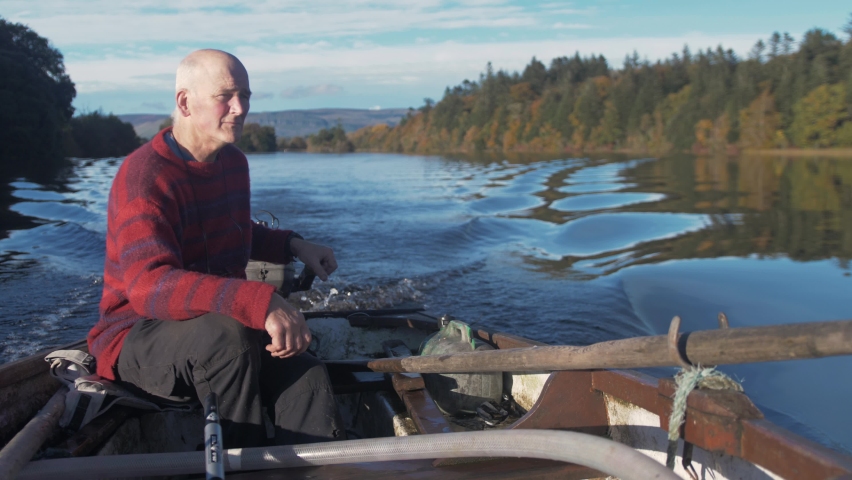 A mature man driving rowboat with outboard engine surrounded by Autumn colours