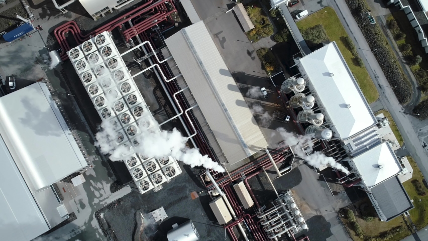 Aerial view of modern geothermal energy power plant working in Iceland. Industrial buildings looks innovative and modern. Hot white steam smoke is coming from chimneys, pipes and ground surface. Royalty-Free Stock Footage #1096173727