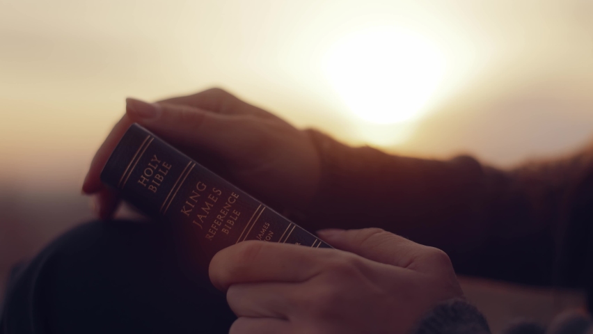 Close-up. A woman opens a Bible, flips through the pages. A girl reads the Bible in the open air, studies the word of God at sunset on top of a mountain. Finding Truth in the Scriptures. Royalty-Free Stock Footage #1096179165