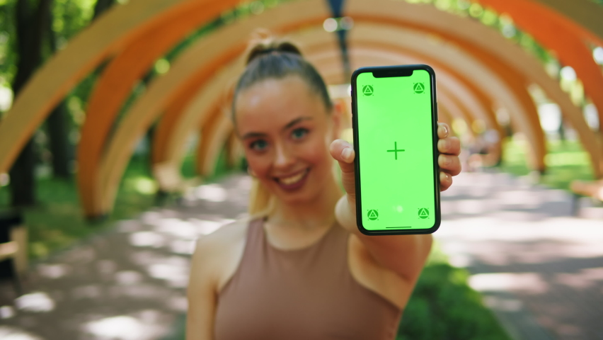 Happy woman holding smartphone with chroma key, smiling female person showing phone and green screen close-up. Cheerful student posing outdoor, looking at camera.  Royalty-Free Stock Footage #1096179487