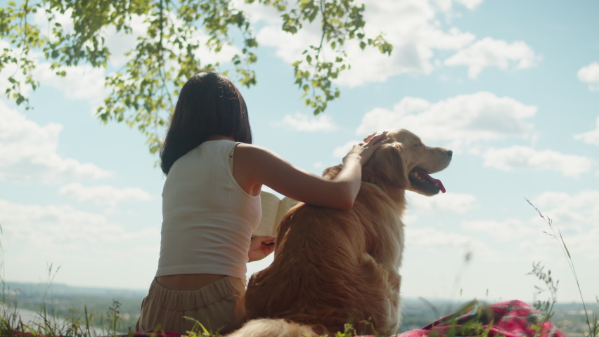 Woman petting golden retriever. Animal trainer relaxing with labrador outdoor, reading book, sitting on rug together. Dog walking service. Happy domestic animals. Royalty-Free Stock Footage #1096179597