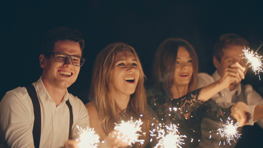 Group of friends holding sparklers in the air at Christmas night outdoors. Christmas party, new year holiday and vacation. Young people celebrate together, enjoying, dance and laugh. Festive mood Royalty-Free Stock Footage #1096187123