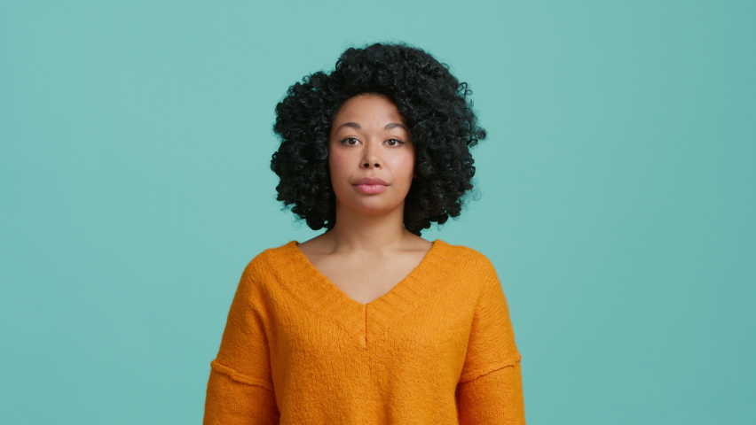 Dont know, who cares. Confused lovely beautiful African American girl shrugging shoulders, looking with uncertain clueless expression, demonstrating indifference doubts. Indoor studio blue background Royalty-Free Stock Footage #1096194891