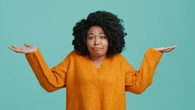 Dont know, who cares. Confused lovely beautiful African American girl shrugging shoulders, looking with uncertain clueless expression, demonstrating indifference doubts. Indoor studio blue background - Powered by Shutterstock - Get 15% off with code: PIKWIZARD15