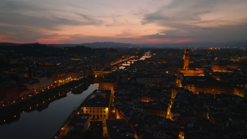 Fly above evening city. Revealing Arno river reflecting colourful twilight sky. Aerial view of historic sight Ponte Vecchio. Florence, Italy Royalty-Free Stock Footage #1096195887