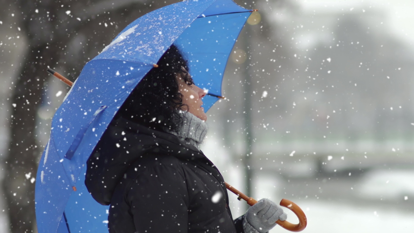 Beautiful young woman with curly hair and an umbrella in snowfall, enjoying the snowflakes on her face