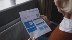 Worried senior woman sitting in wheelchair by radiator at home looking at energy bill - shot in slow motion - Powered by Shutterstock - Get 15% off with code: PIKWIZARD15