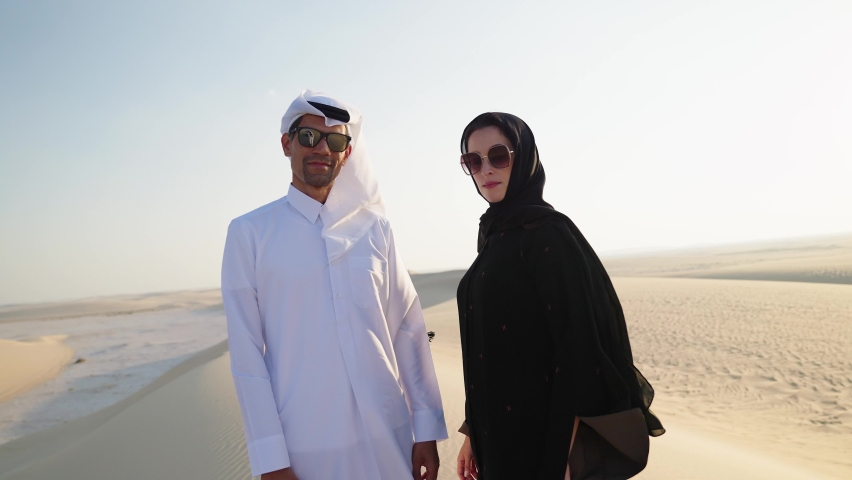 Muslim couple in traditional Abaya dress and clothing stand along the sand dunes in the desert of Qatar
