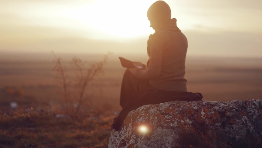  Young woman sitting alone on a rock in a field, reading the bible, praying in nature with an incredible view, watching a beautiful sunset in an autumn evening, peace and tranquility, faith, God's  | Shutterstock HD Video #1096208473