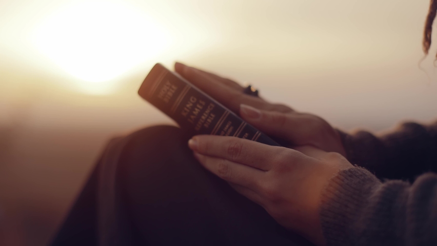  A woman reads a book at sunset. A girl reads the Bible in the open air. Female holding bible in hands and studying word of God at sunrise on top of mountain. Finding Truth in the Scriptures. | Shutterstock HD Video #1096208475