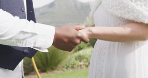 Video of midsection of diverse bride and groom holding hands and walking at outdoor wedding. Marriage, love, happiness and inclusivity concept.