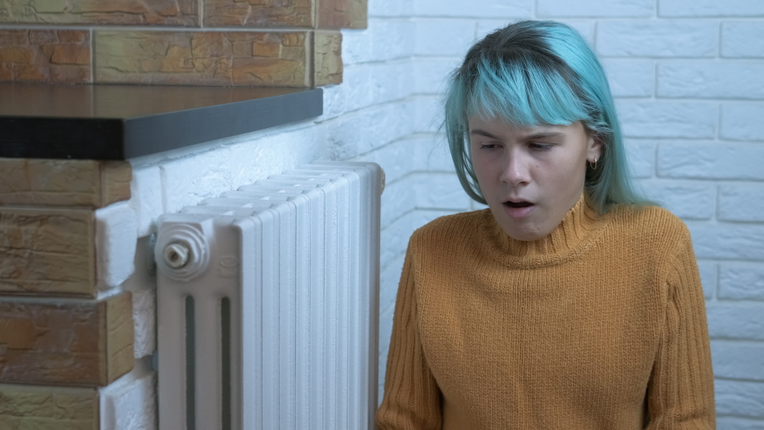 Girl warming in unheated apartment. A stressed young girl warming in unheating apartment on the floor. A concept of cold winter time and rising of heating costs.