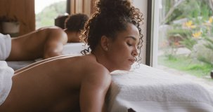 Video of relaxed diverse couple lying with eyes closed on massage tables at health spa. Vacation, togetherness, relaxation, health, happiness and inclusivity concept.