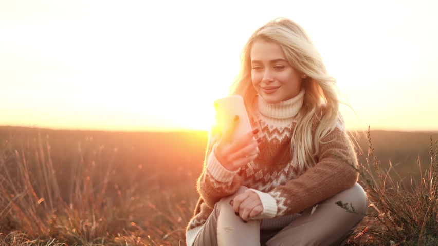 Charming young traveler have a video call with beautiful sunset in the mountains. Young blond woman recording video for her social media blog.