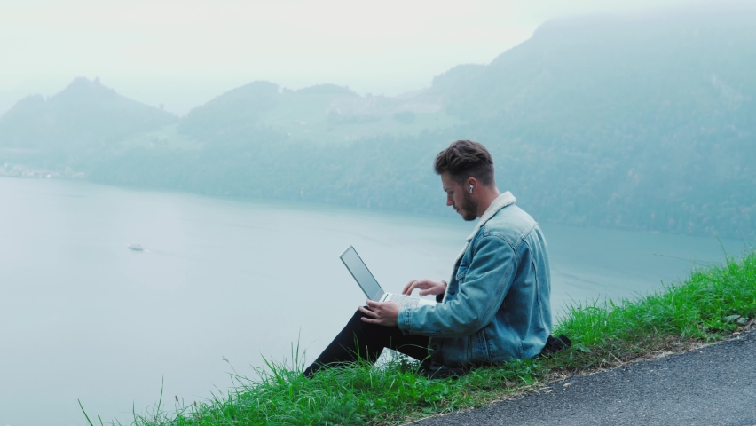 Handsome man typing on notebook computer keyboard. Man work out of office on epic nature landscape, feeling excitement, getting good news, feeling euphoria, raising arms. Feel of success, victory, joy