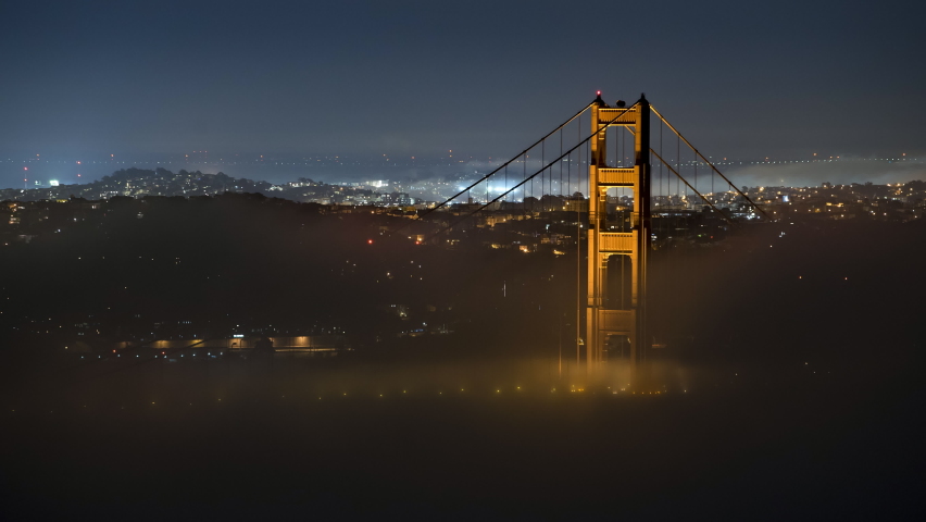 Aerial Lockdown Time Lapse Shot Of Clouds Moving By Golden Gate Bridge In Illuminated Residential City At Night - San Francisco, California
