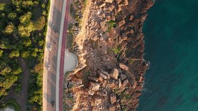 Aerial drone footage of the rocky coast by the sea in Cascais town at sunset, Lisbon, Portugal. Top down view of the coastal road near the natural landmark Boca do Inferno in Cascais city. 