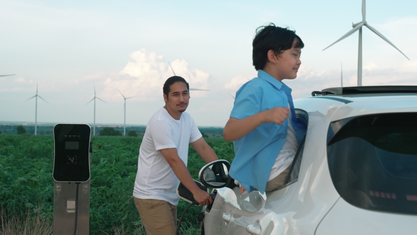 Concept of progressive happy family enjoying their time at wind farm with electric vehicle. Electric vehicle driven by clean renewable energy from wind turbine generator for charging station. Royalty-Free Stock Footage #1096232819