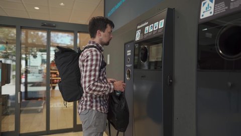 Male returns plastic bottles, reusable containers to reverse vending machine in Munich, Germany supermarket. Man using bottle deposit point. Automatic bottle recycling machine for collection plastic. の動画素材