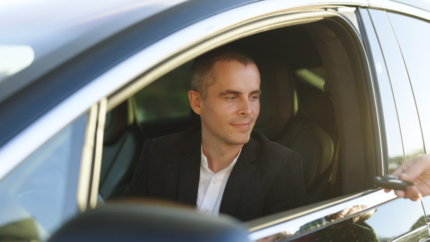 Happy man taking car key from dealer in auto show or salon. Car dealer giving key to new car owner. Businessman sitting behind steering wheel at car. Driving, safety and people concept Royalty-Free Stock Footage #1096240261