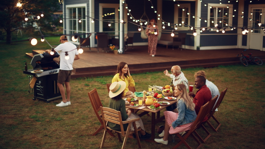Group of Multiethnic Diverse People Having Fun, Communicating with Each Other and Eating Barbecue at Outdoors Dinner. Family and Friends Gathered Outside Their Home on Warm Summer Afternoon.