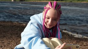 Portrait of a happy caucasian teenage hipster girl with pink braids using a smartphone on a deserted beach.Summer concept.Generation Z style.Social media concept.