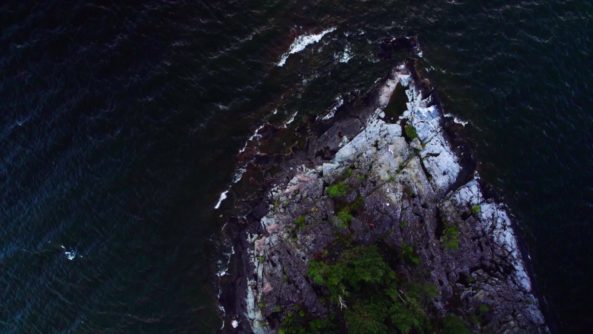 Evening top down view over crashing waves against the rocky coastline of an island with pine trees, dark lake in Säffle Vänern lake Sweden. Nature scenery background in 4K resolution
