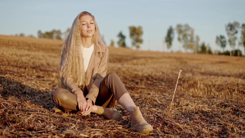 portrait beautiful charming young woman girl lady long-haired blonde sitting in autumn field alone, smiling happily, enjoying life, peace, relaxed in sunlight
